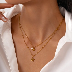 Detail of gold double-layer necklace featuring starfish and shell charms with a pearl