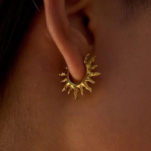 Gros plan de créoles rayons de soleil en or 18 carats avec texture métal liquide