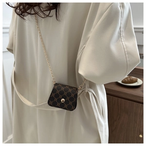 Detail of a dark brown mini crossbody bag with gold chain strap on a white dress
