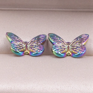 Dettaglio macro di orecchini a farfalla iridescenti con trama alare su velluto rosa