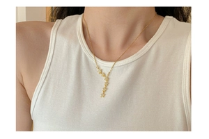 Detail of gold titanium star pendant necklace featuring shimmering tassels on a model