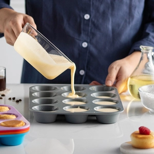 Gray silicone 12-cup muffin pan being filled with batter in a professional kitchen setting