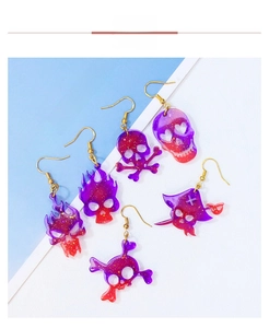 Detail of purple gradient acrylic skull earrings with gold glitter on a blue background