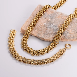 Detail of gold woven chain necklace and bracelet set displayed on a stone background