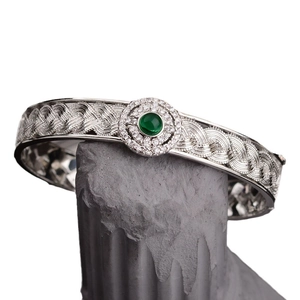 Silver woven lace bracelet with green gemstone and diamond accents on stone base