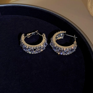 Macro detail of silver C-shaped earrings with sparkling cubic zirconia on blue velvet