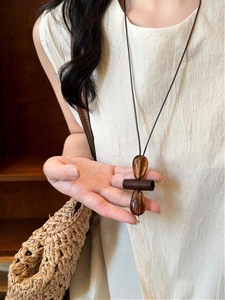 Macro detail of amber resin teardrop pendant with wooden geometric beads on long cord