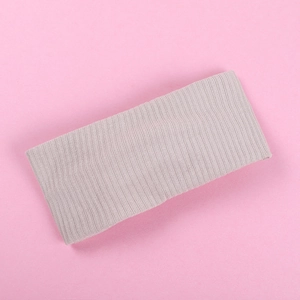 Detailed texture of the light beige ribbed knit baby headband on a pink background