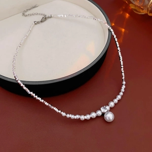 Macro detail of silver necklace with crushed silver beads, zircon, and round pearl drop
