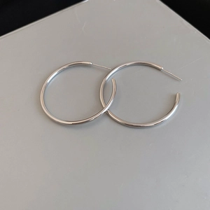 Flat lay of large minimalist silver hoop earrings on a light gray background