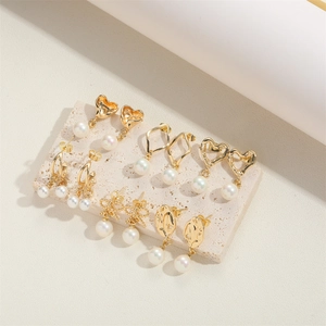 Close-up of gold plated pearl earrings with heart, diamond, and bow designs on travertine