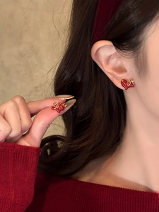Detail showing red heart enamel earring with gold-plated edges worn by a model