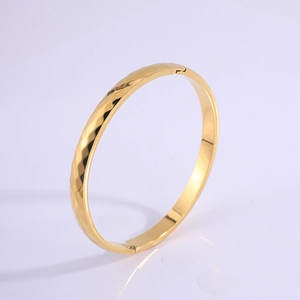 Macro detail of gold titanium steel bangle showing diamond-cut texture and mechanical clasp