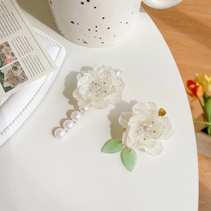 Eleganti fermagli per capelli con fiori di camelia bianchi e perle su scrivania bianca