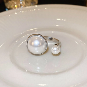 Detailed view of double pearl open ring with silver finish on white porcelain plate