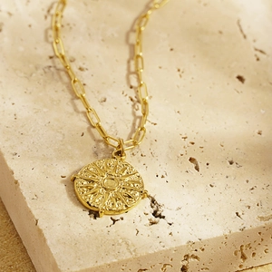 Collier à médaillon solaire doré avec chaîne trombone sur un fond de pierre neutre