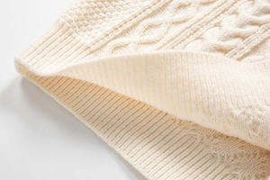 Dettaglio della trama a trecce e polsino a coste su maglione girocollo bianco caldo