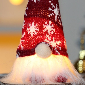 Close-up of a glowing red knitted Christmas gnome with warm LED light and snowflake pattern