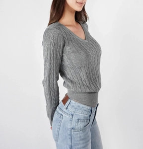 Detailed close-up of grey cable-knit sweater with V-neck and ribbed cuffs design