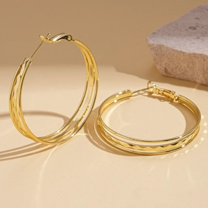 Detail of gold layered hoop earrings with textured diamond patterns on stone background