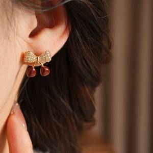 Gros plan d'une femme portant des boucles d'oreilles nœud cerise dorées et zircons