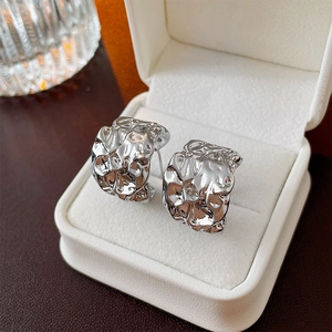 Macro shot of silver metallic C-shape earrings with irregular pleated texture in a gift box