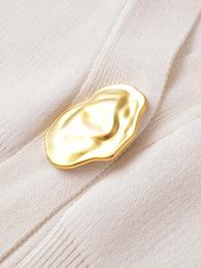 Macro shot of an organic gold metal button on an off-white ribbed knit cardigan texture