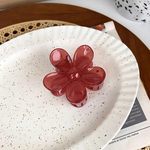 Close-up of a translucent red flower hair claw clip on a stylish ceramic plate