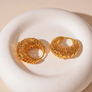 Detailed macro shot of gold-plated woven hollow geometric hoop earrings on a white tray