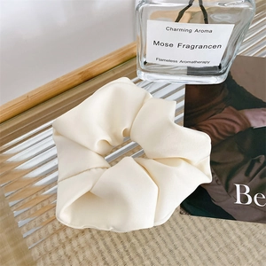 Detail view of a beige matte satin scrunchie on a decorative tray with aesthetic background