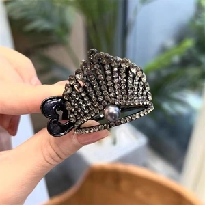 Close-up of crown-shaped hair claw clip with dark grey rhinestones and a central grey pearl