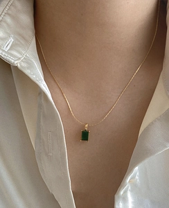 Close-up of elegant gold chain with square emerald green zircon pendant on white satin
