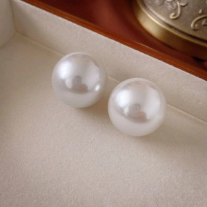 Macro shot of a smooth white round pearl earring set on a beige velvet jewelry box