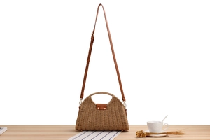 Detail of light brown paper rope woven bag with adjustable leather strap on wooden surface