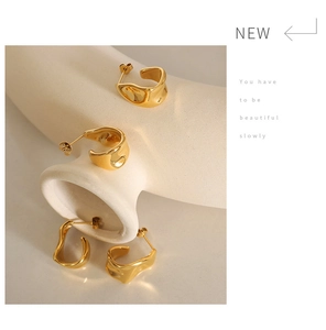 Détail de boucles d'oreilles dorées en forme de C sur présentoir de vase en céramique