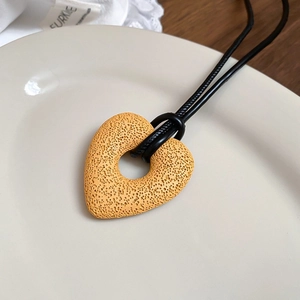Macro shot of yellow heart pendant with textured honeycomb finish on black leather cord