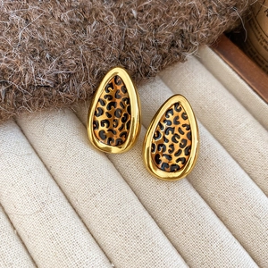 Detail of leaf-shaped leopard print earrings with gold frames on a beige tray