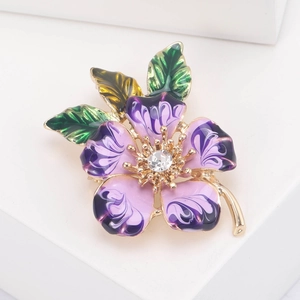 Macro shot of purple enamel flower brooch with golden metal base and crystal center