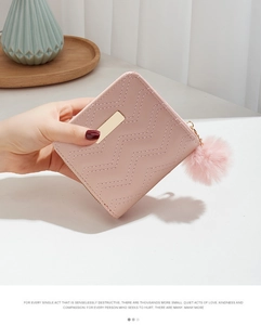Mini portefeuille rose matelassé avec plaque dorée et pompon doux tenu à la main