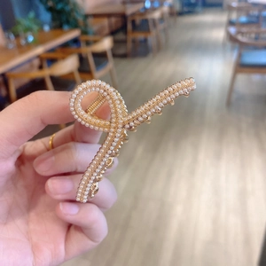 Close-up of a gold metal hair claw clip with elegant pearls held in hand for detail