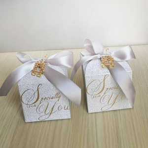 Sparkly silver wedding favor box with ribbon and gold character charm on wood background