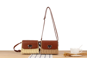 Detail of paper straw crossbody bags in beige and brown with leather flaps on wooden surface