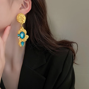 Detail of vintage matte gold floral earrings with blue gems worn by a model