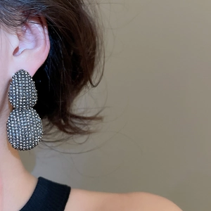Detail view of large oval rhinestone stud earrings with grey stones on a fashion model