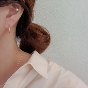 Detail of model wearing gold hoop earrings, pearl studs, and a delicate silver necklace