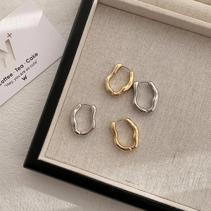 Flat lay of irregular wave-shaped hoop earrings in gold and silver on a linen tray