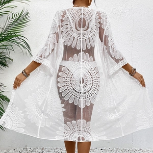 Close-up of white lace floral embroidery on a sheer beach cover-up with wavy edges