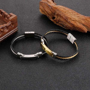 Detail of woven leather bracelets with silver and gold steel rectangular plates on wood