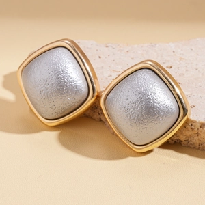 Macro view of geometric square stud earrings with gold frames and textured silver inlay