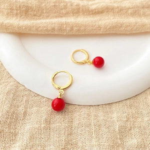 Detail of red bead earrings with 18K gold-plated hoops on textured linen background